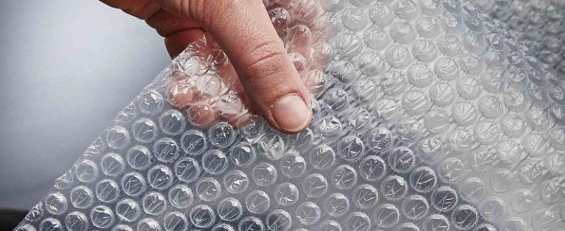 Close-up of a hand touching clear bubble wrap covered in uniform air filled bubbles.