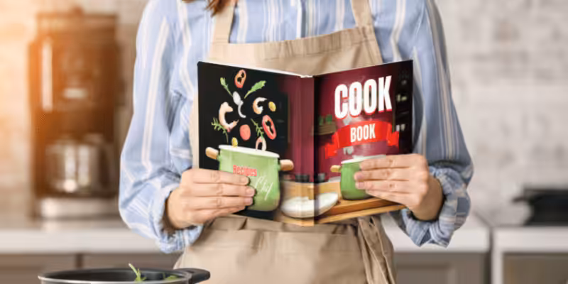 Chef holding a professionally printed colorful cook book in kitchen, showcasing high-quality book printing for recipe publications.