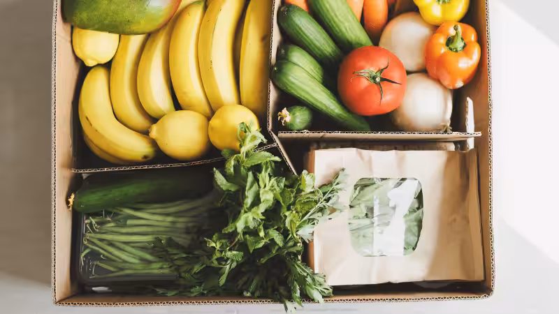Frische-Produkt-Lieferbox mit umweltfreundlicher Verpackung, bestehend aus Obst, Gemüse und Kräutern in einem Kartonbehälter.