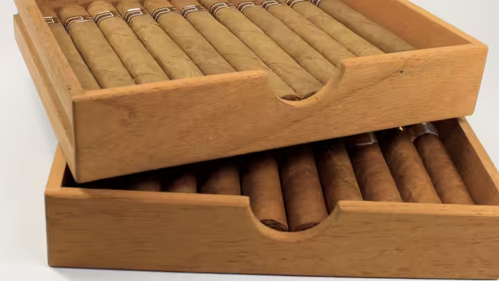 Two-layer wooden box for cigars with finger cutouts, holding neatly arranged cigars in both top and bottom drawers, showcasing functional storage design.