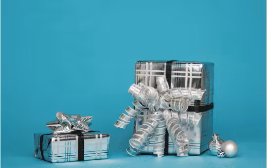 Two uniquely shaped gift boxes wrapped in silver plaid paper with black ribbons and curly bows, on a turquoise background.