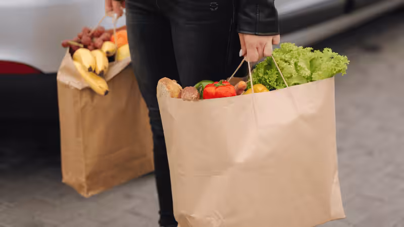Woman carrying paper grocery bags with vegetables and fruits