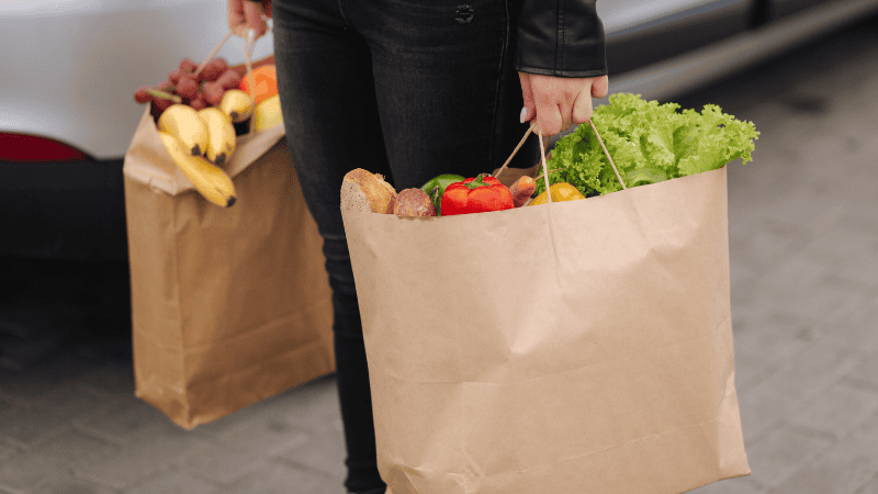 Woman carrying paper grocery bags with vegetables and fruits