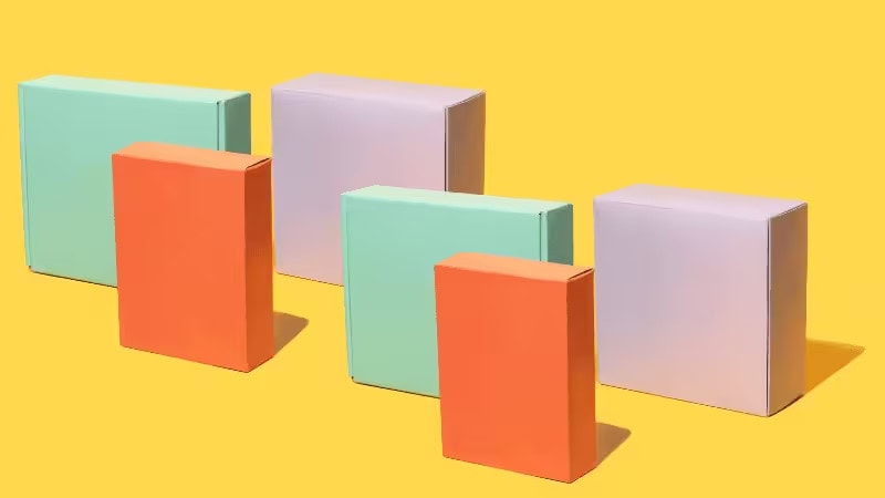 Three pastel-colored rectangular boxes (mint green, lavender) and three orange boxes are arranged standing upright in two rows on a yellow background.