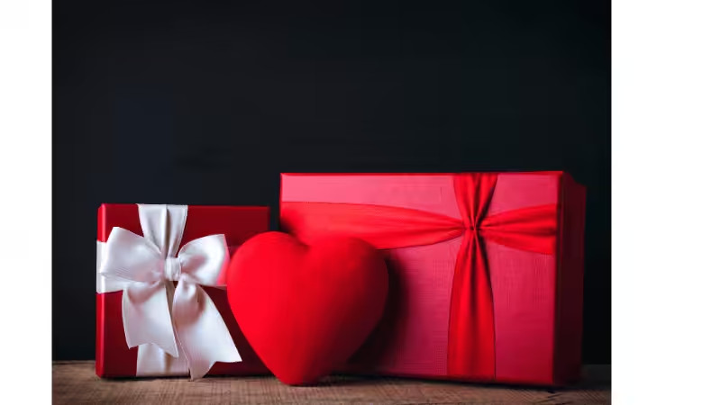 Two red gift boxes with satin bows, paired with a plush red heart, on a dark wooden surface.