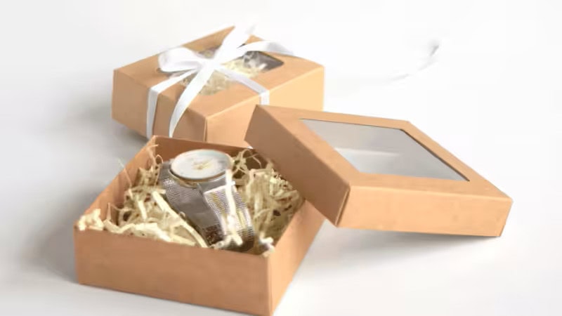 Offene und geschlossene Kraftpapier-Geschenkboxen mit Sichtfenster, gefüllt mit Papierschnipseln.