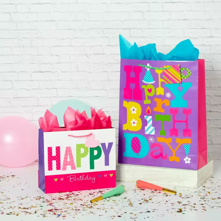 Bunte Geschenktüten aus Papier mit der Aufschrift „Happy Birthday“ und Seidenpapier.