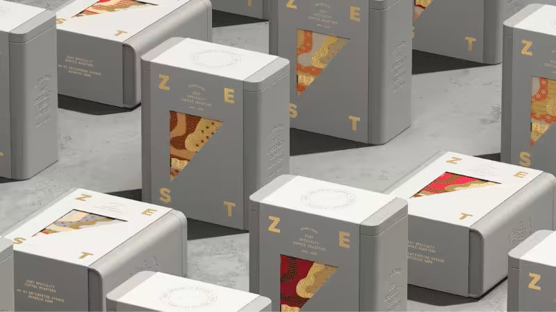 Gray metal window gift box packaging for ZEST specialty coffee, featuring triangular transparent windows, gold typography, and colorful patterned interior designs.