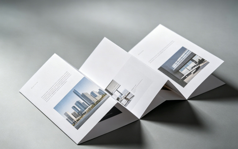 Minimalist accordion-fold brochure mockup with cityscape and office interior photos, clean white design on neutral background.