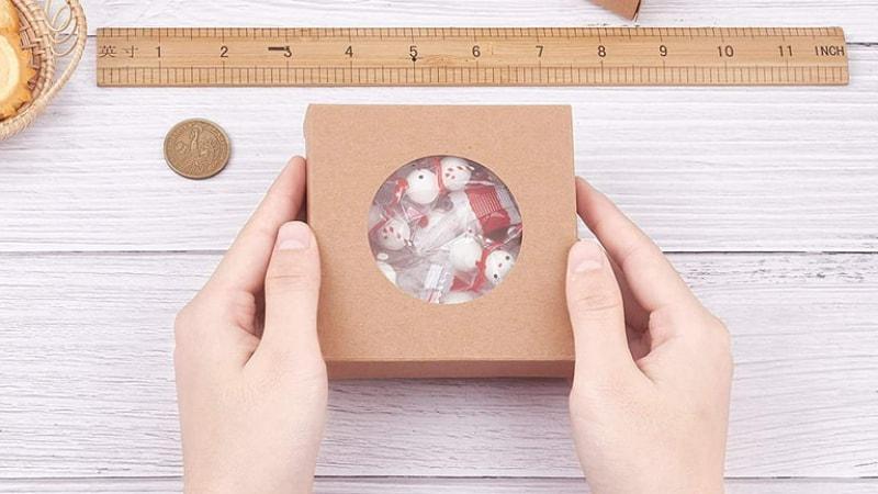 Kraft paper square window box packaging with a round clear window, holding festive candies inside.