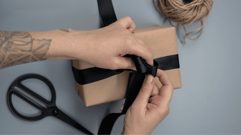 A person tying a black ribbon on a gift box