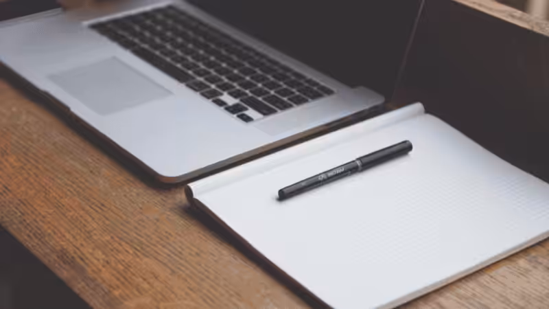 a notebook, pen, laptop on a table