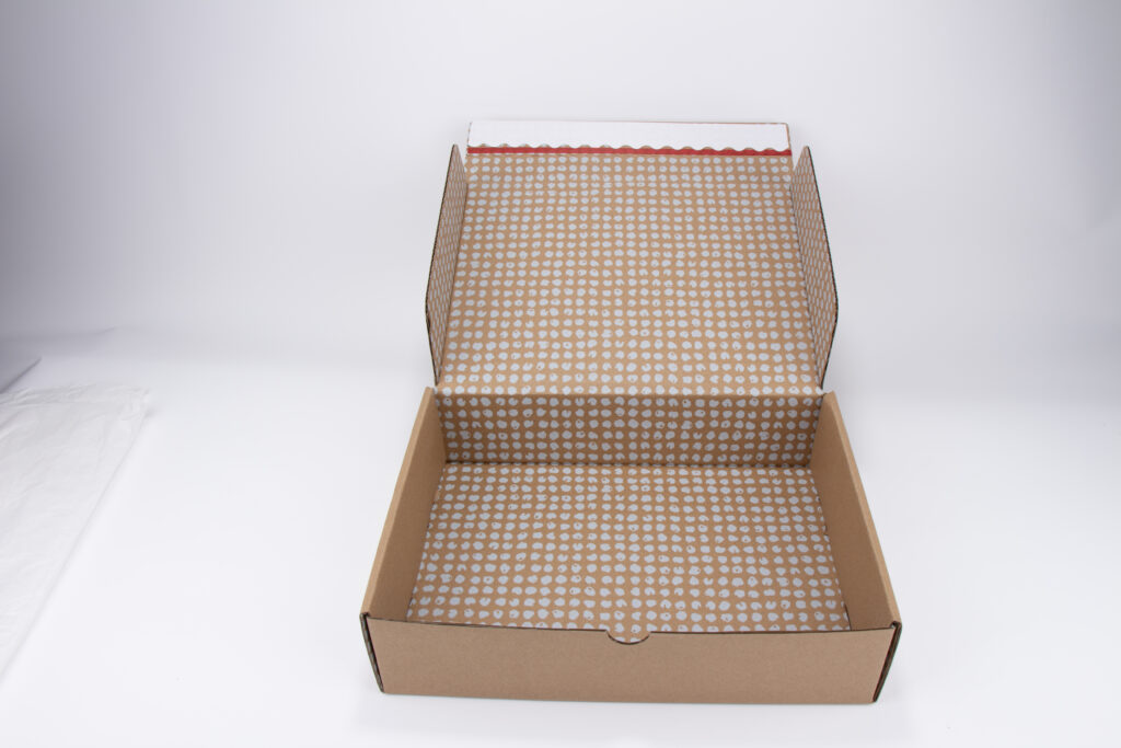 Open custom printed kraft mailer box with white dot pattern interior, corrugated shipping packaging box for e-commerce