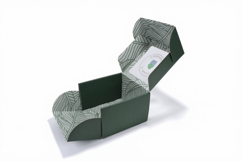 Open custom printed mailer box, dark green exterior with tropical leaf pattern interior, branded packaging on white background